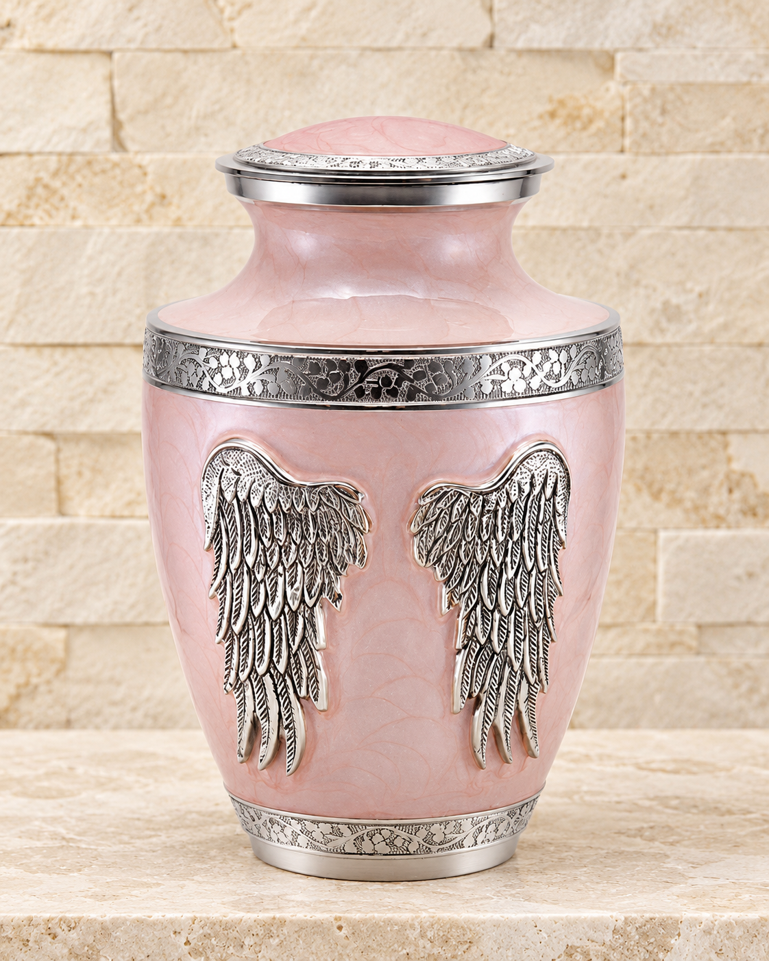 pink angel wings individual cremation urn on cream stacked stone, portrait product photograph